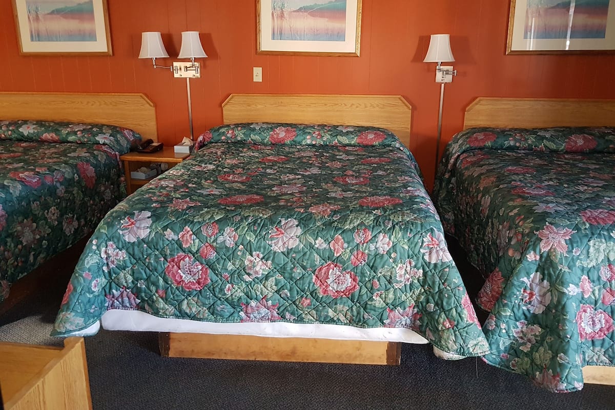 A hotel room with two beds, each with floral bedding, wooden headboards, and bedside tables with lamps.