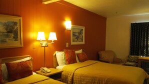 Quarto de hotel com duas camas, mesa de cabeceira com telefone, duas luminárias na parede, um quadro e uma cadeira.