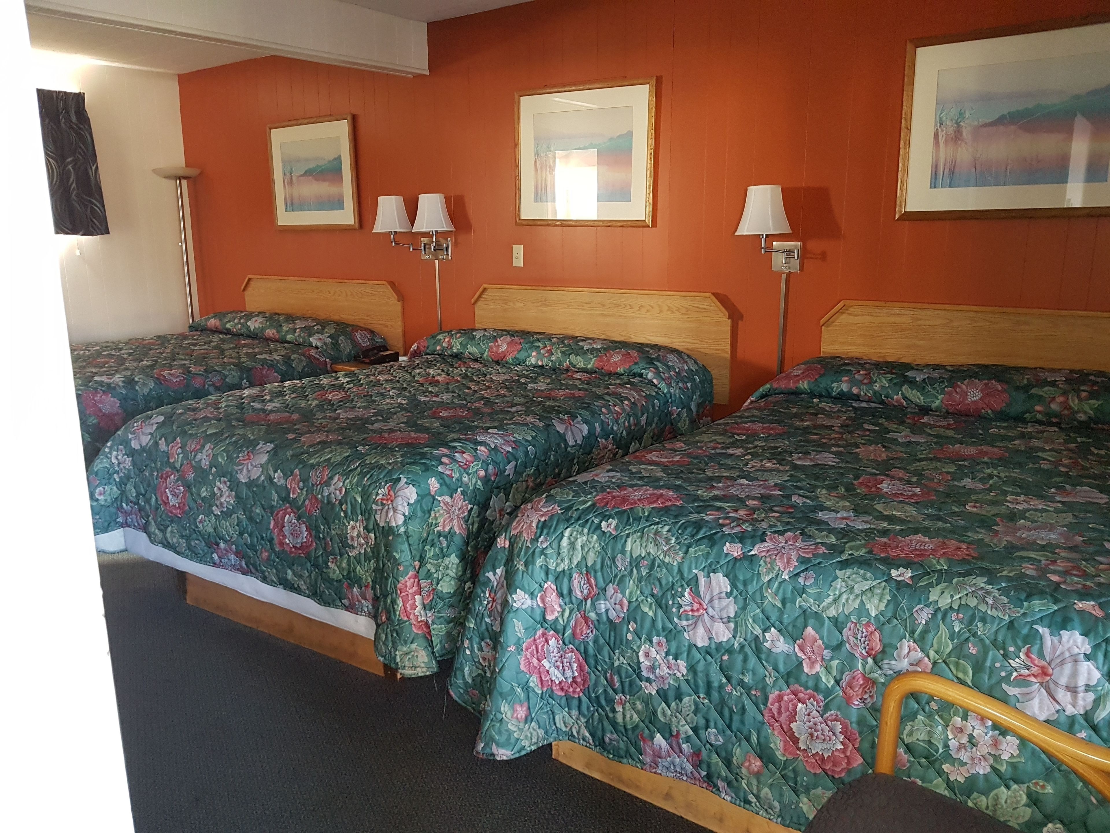 Una habitación con tres camas, cada una con ropa de cama estampada, cabeceros de madera y lámparas de pared.