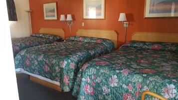 Una habitación con tres camas, cada una con ropa de cama estampada, cabeceros de madera y lámparas de pared.