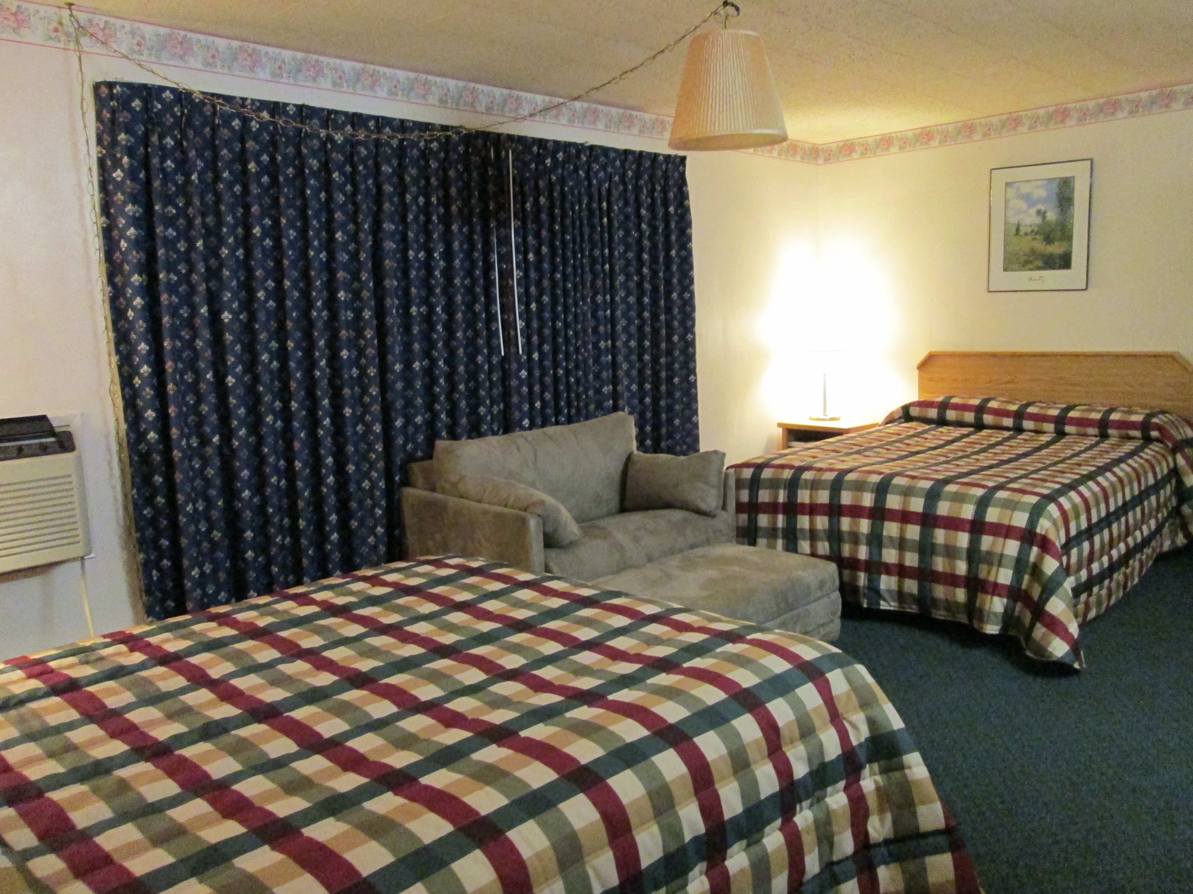 A hotel room with two beds, a sofa, a lamp, and a painting on the wall.