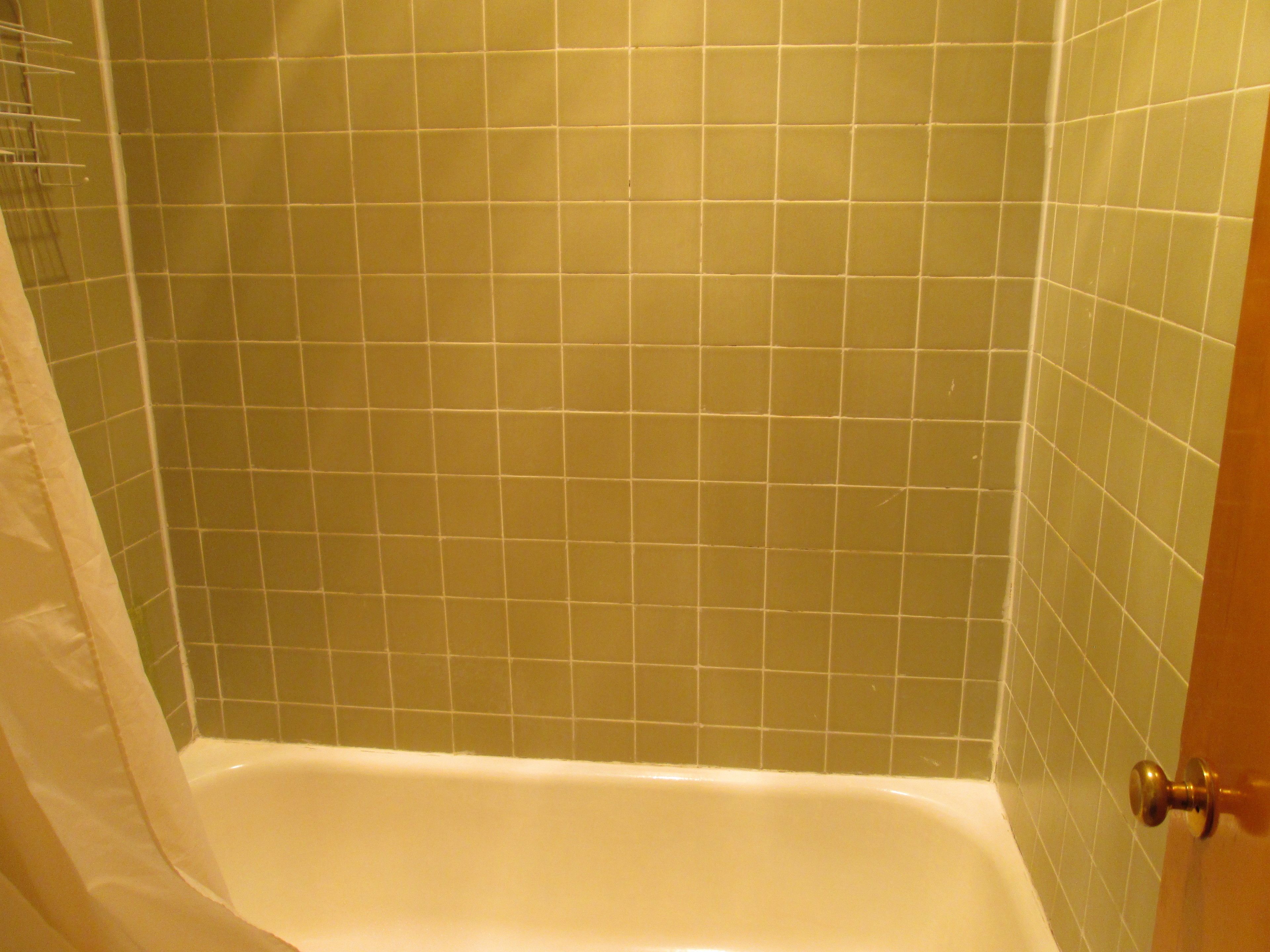 Une salle de bain avec une baignoire, des murs recouverts de carreaux verts et un rideau de douche blanc.