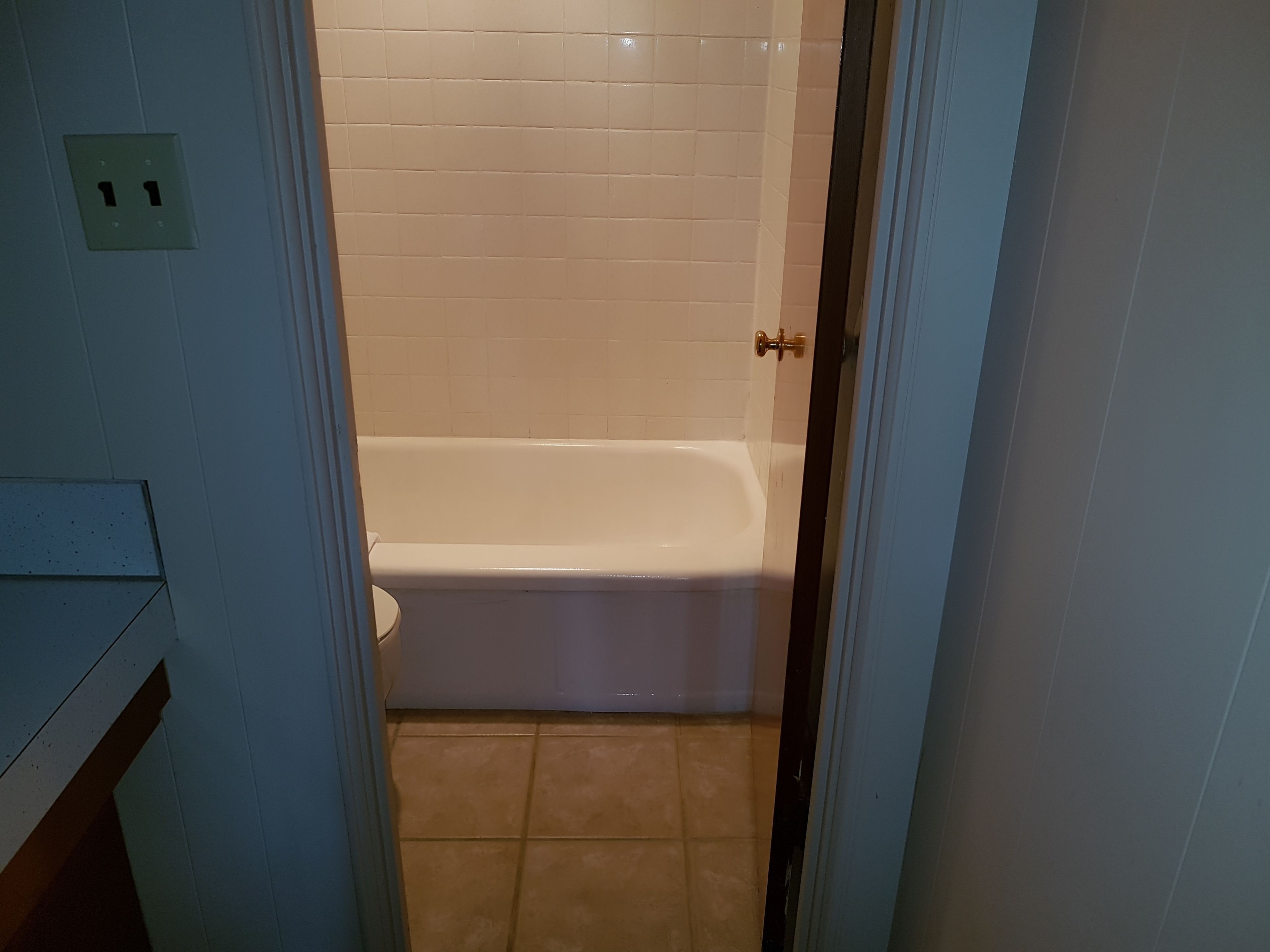 Une salle de bain avec une baignoire blanche, des carreaux de couleur beige et une porte dotée d’une poignée en laiton.