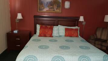A hotel room with a bed, two bedside tables, a chair, a painting, and a wall-mounted lamp.