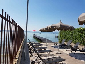 Ein Strandbereich mit Liegestühlen, Sonnenschirmen und einem Holzsteg, der sich ins Wasser erstreckt.