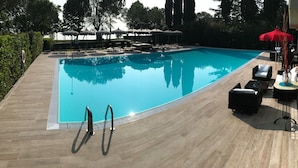 A swimming pool with a wooden deck, lounge chairs, and umbrellas. - Alexandra Stay Residence (Sirmione)