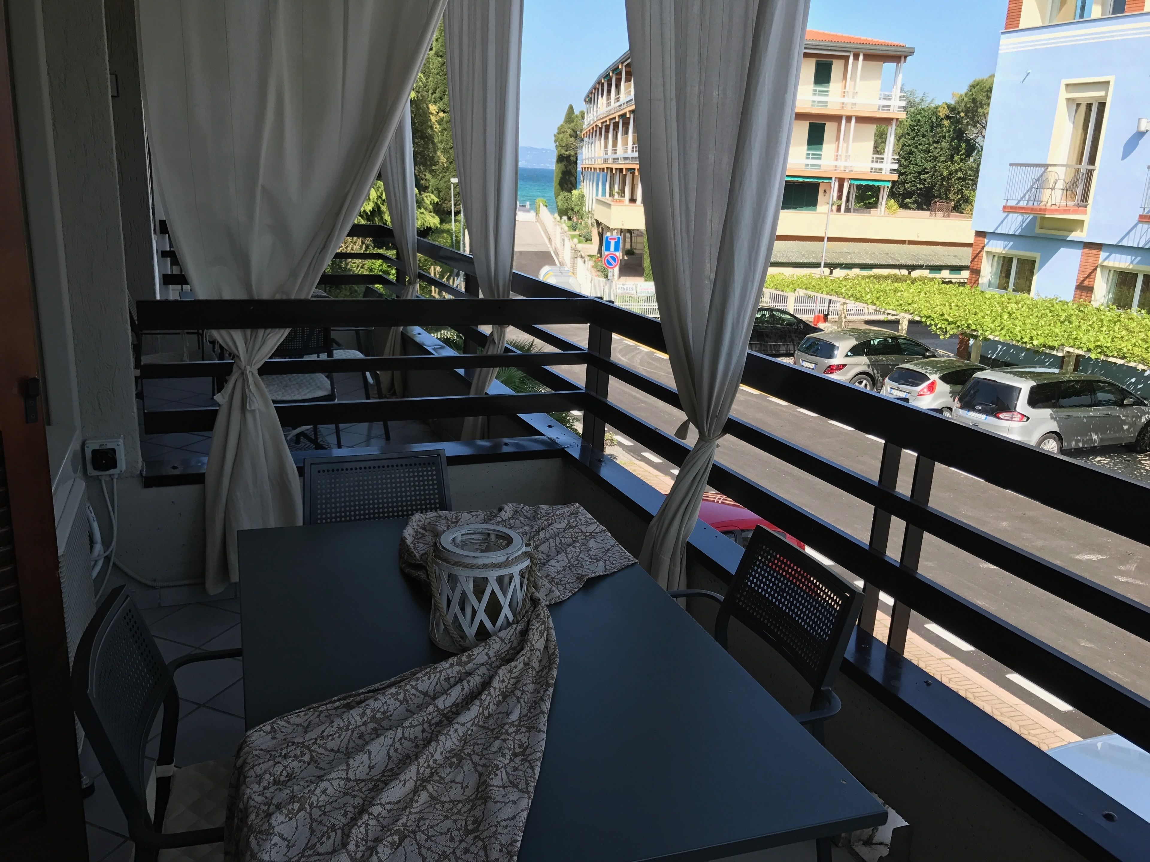 A balcony with a table, chairs, and a view of a street with parked cars and buildings.