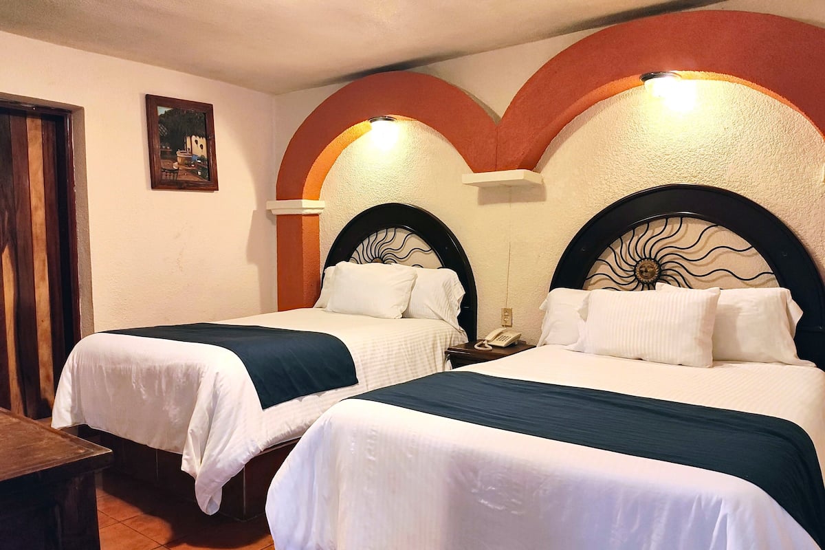 Ein Hotelzimmer mit zwei Betten, jeweils mit einem sonnenähnlichen Design an der Kopfteil, einem kleinen Nachttisch mit Telefon und einem Bild an der Wand.
