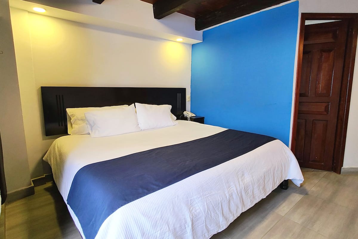 Ein ordentlich bezogenes Bett mit einer schwarz-weißen Tagesdecke, einem Nachttischtelefon und einer Holztür in einem Zimmer mit blauen Wänden und Holzböden.