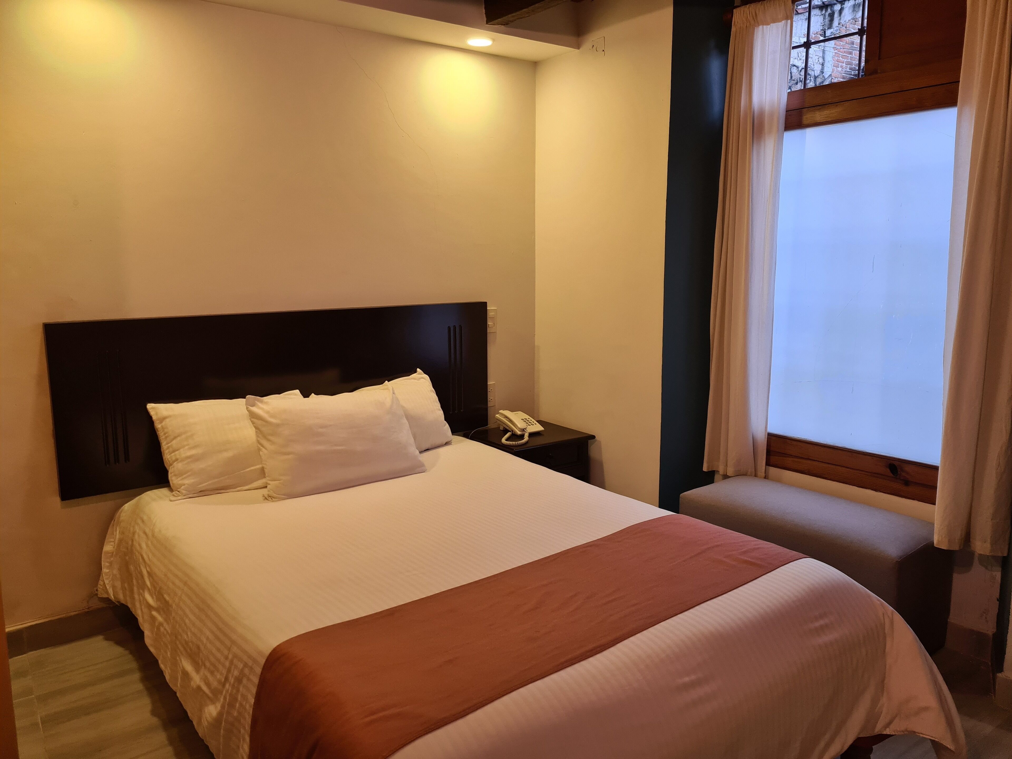 Ein Hotelzimmer mit einem Bett, einem Nachttisch mit Telefon und einem Fenster mit Vorhängen.
