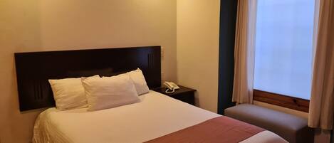 Ein Hotelzimmer mit einem Bett, einem Nachttisch mit Telefon und einem Fenster mit Vorhängen.