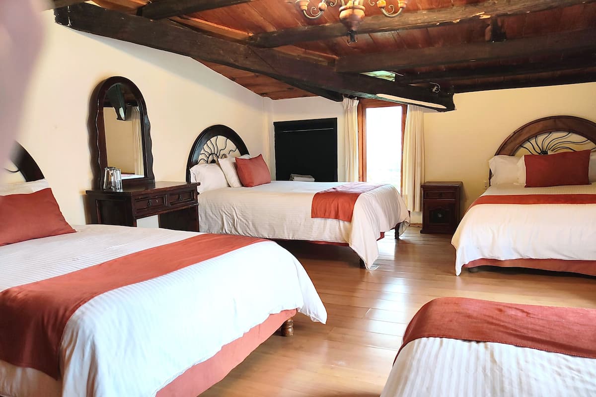 Ein Hotelzimmer mit drei Betten, Holzböden, einem großen Spiegel und einer Decke mit freiliegenden Balken.