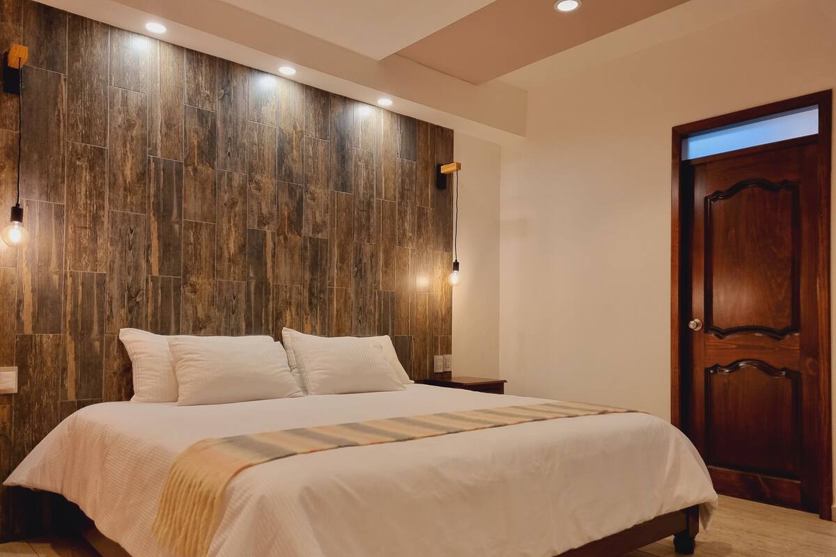 Ein Schlafzimmer mit einem hölzernen Kopfstück, einem großen Bett mit weißer Bettwäsche und einer Holztür.