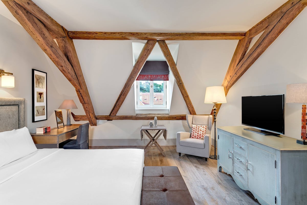 A bedroom with a large bed, a desk, a chair, a TV, and a cabinet. There is a window with a view of the outside.