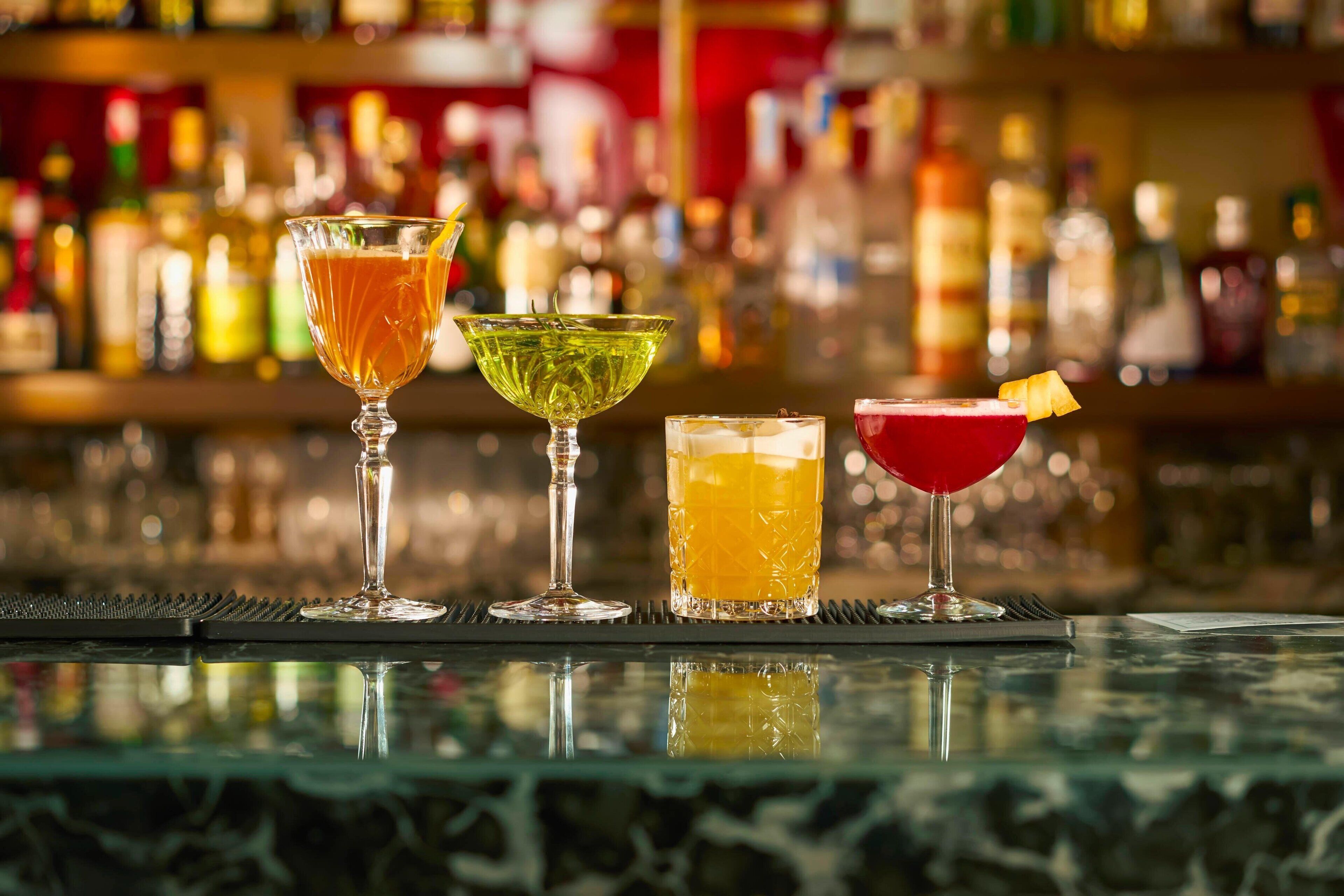 A bar with four different cocktails on a glass bar mat.