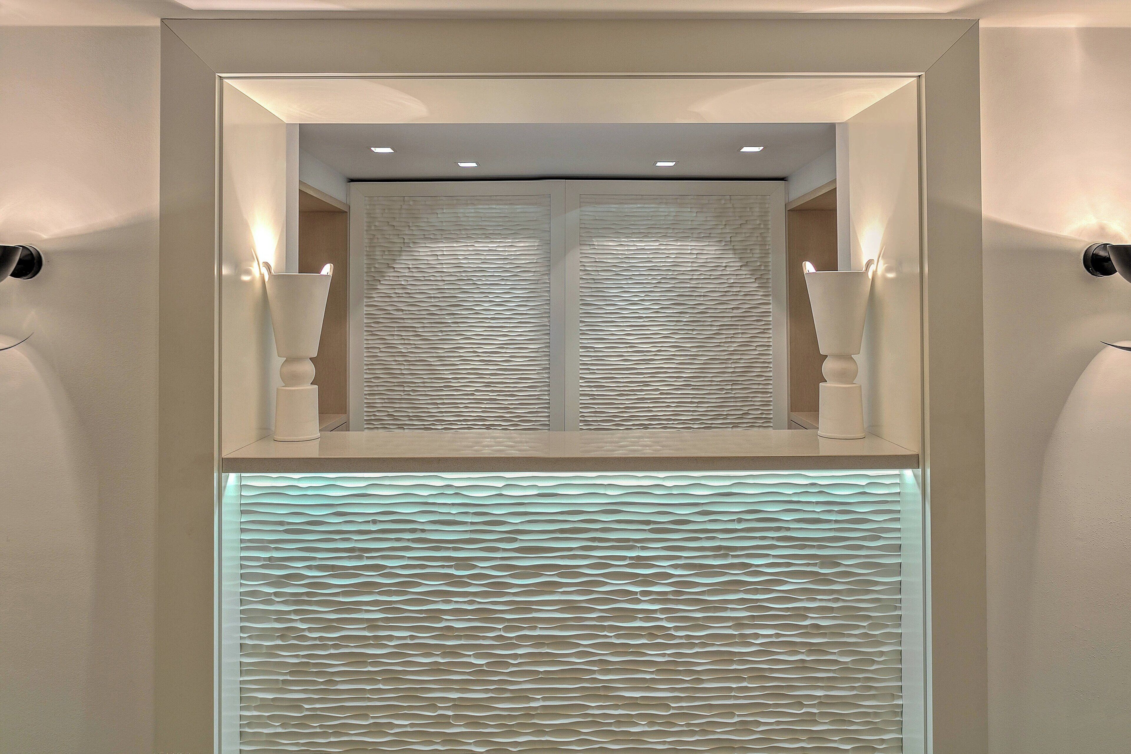 Un baño moderno con un espejo grande, iluminación empotrada y paneles de pared texturizados.