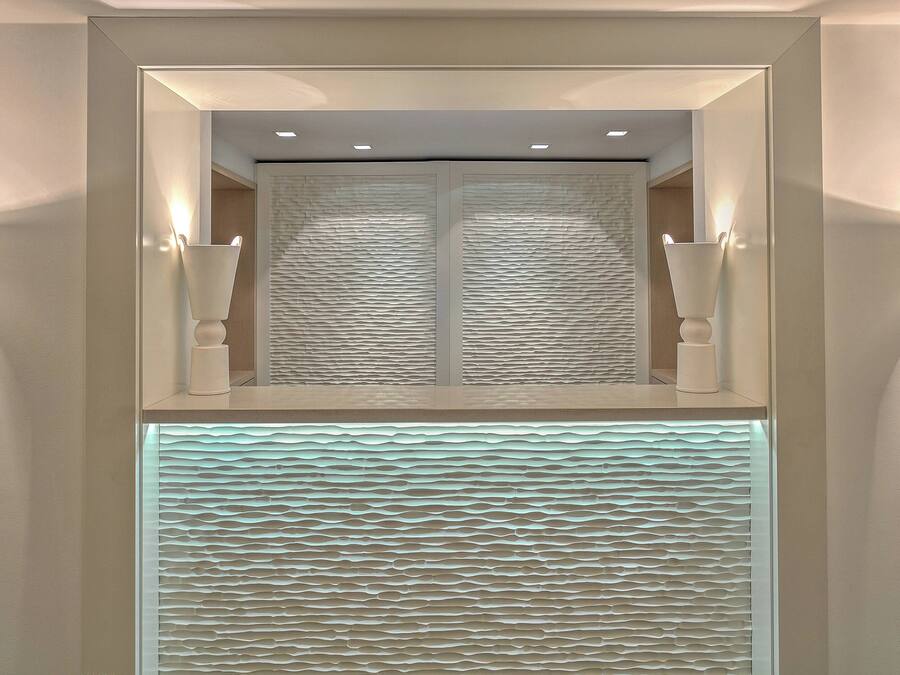 Un baño moderno con un espejo grande, iluminación empotrada y paneles de pared texturizados.
