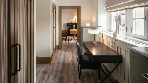 Un pasillo estrecho con suelo de madera que conduce a un comedor con una mesa y sillas.