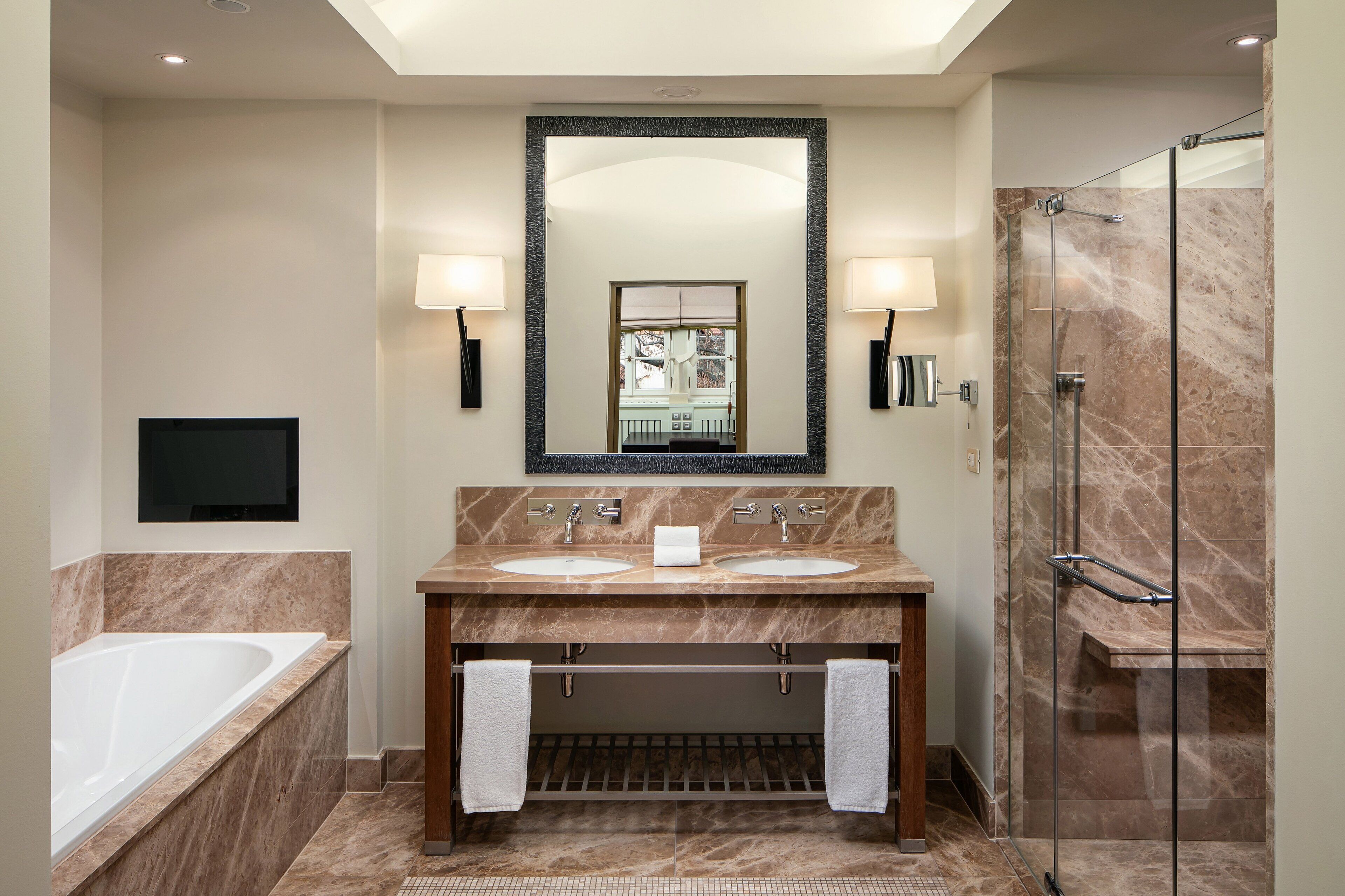 A modern bathroom with two sinks, a large mirror, a bathtub, and a glass-enclosed shower.