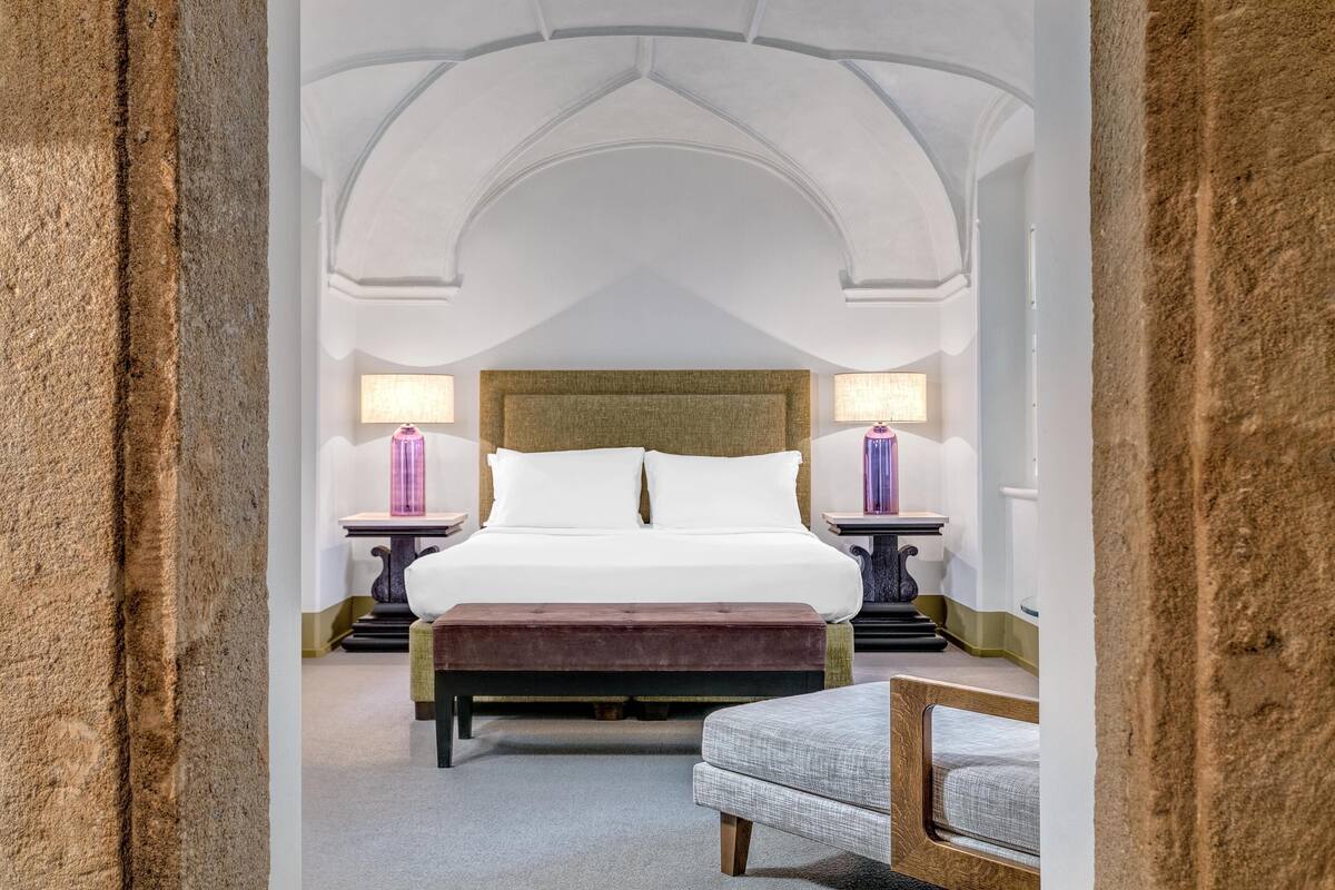 A bedroom with a large bed, two bedside tables, a bench, and an arched ceiling.