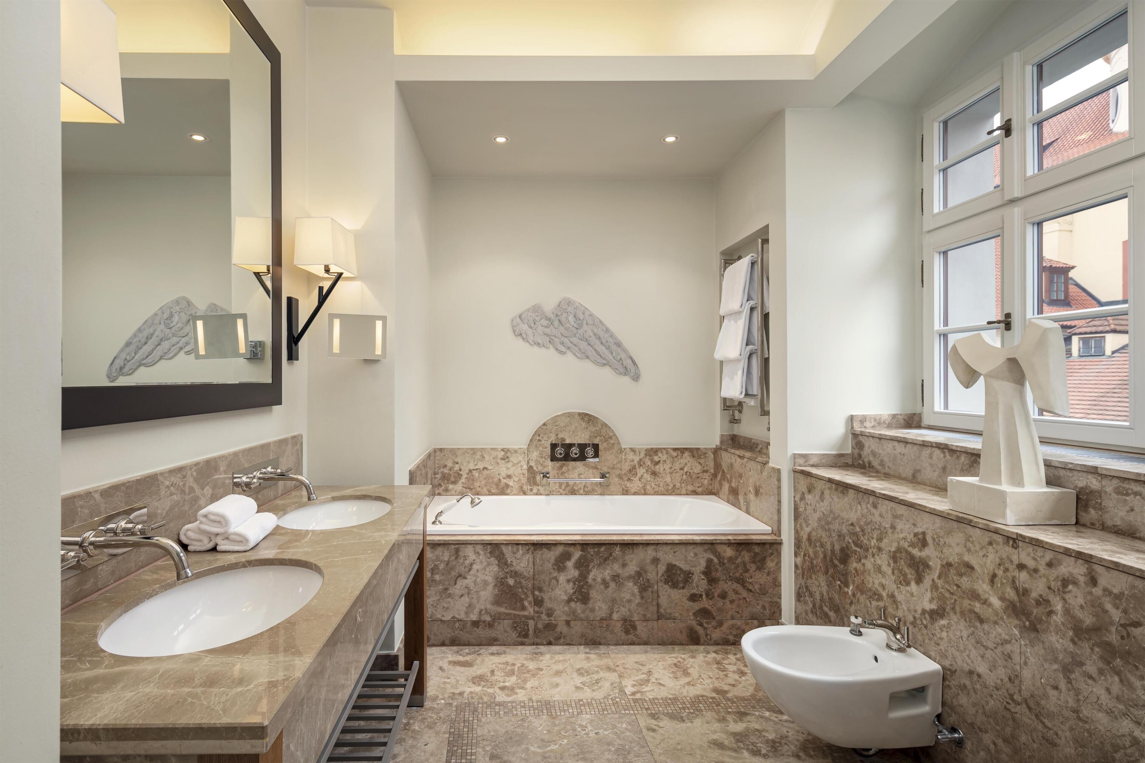 A modern bathroom with two sinks, a bathtub, a bidet, and a large mirror.
