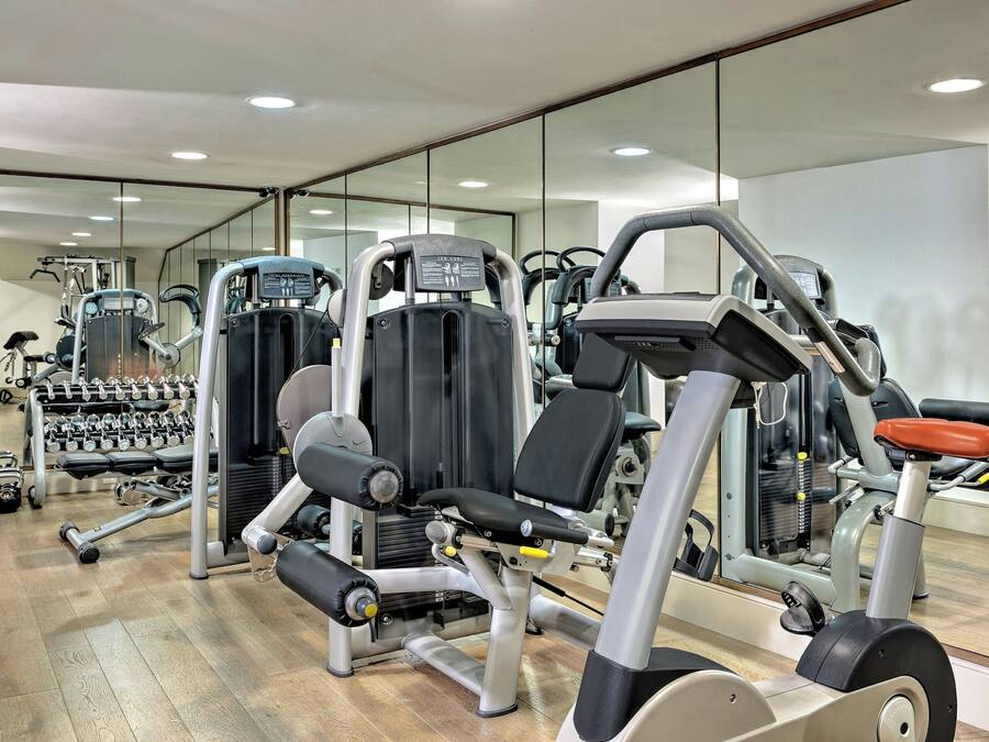 Un gimnasio con diversas máquinas de ejercicio, pesas y un espejo grande.