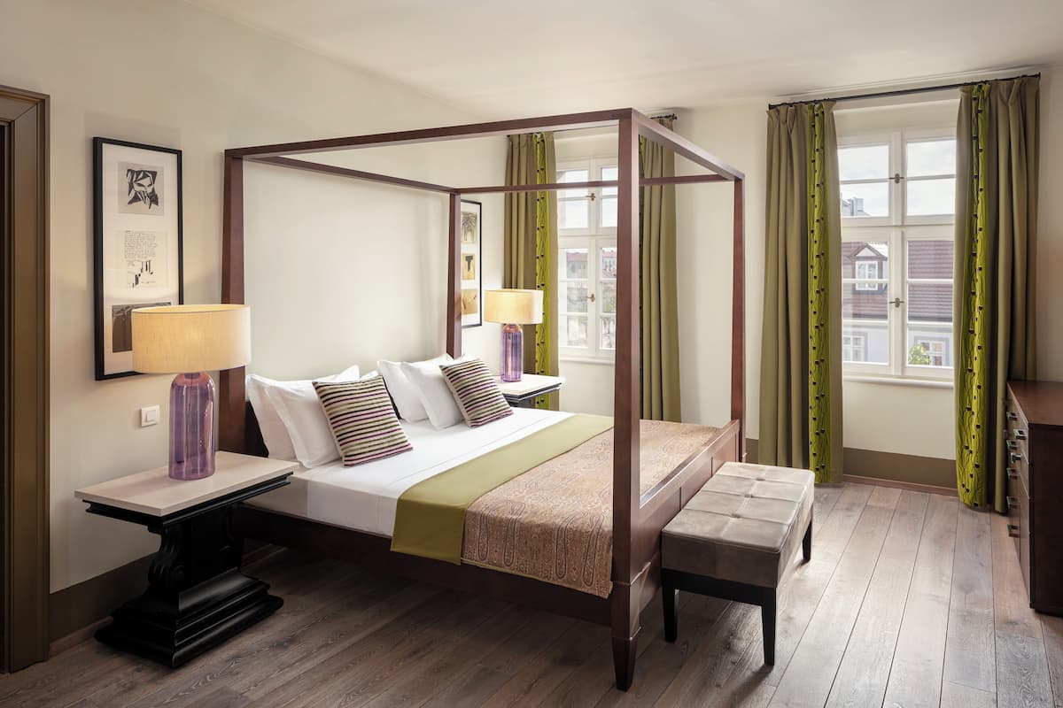 A four-poster bed with a bench, bedside tables, and a view of the outside through a window.