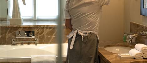 Una persona ajustando una lámpara en un baño con encimera de mármol, una bañera y un perchero.