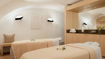 A spa room with two beds, a bench, a mirror, and a counter with towels and toiletries.