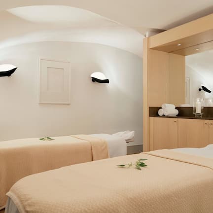 A spa room with two beds, a bench, a mirror, and a counter with towels and toiletries.