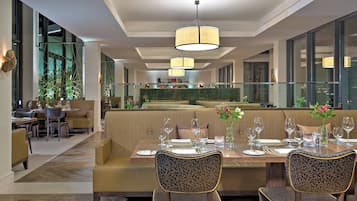 A modern dining area with a long table set for four, surrounded by cushioned seating.