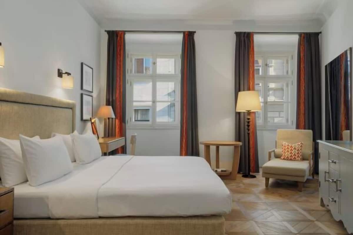 A hotel room with a bed, a chair, a desk, a lamp, and a wardrobe.