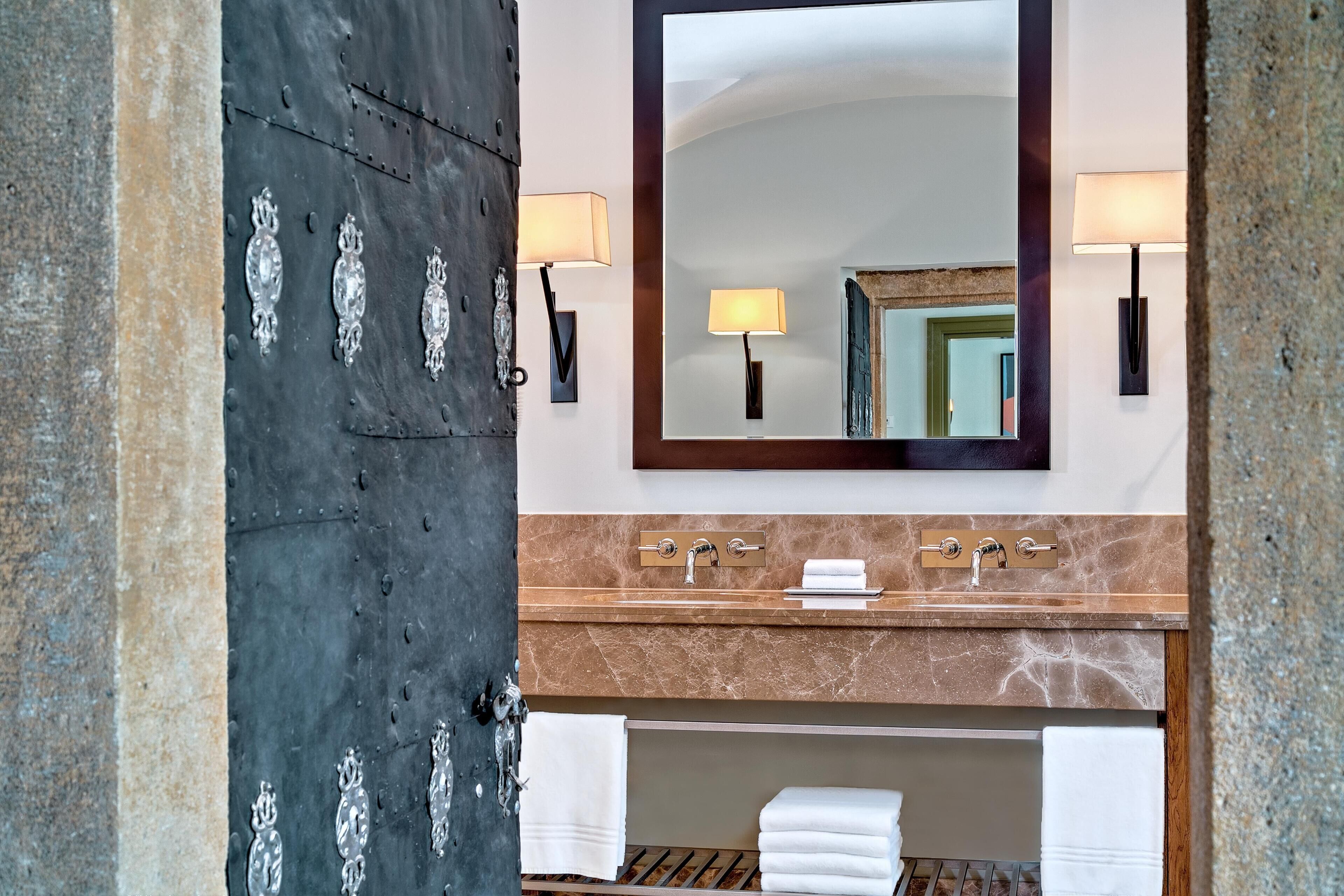 Une salle de bain avec un lavabo en marbre, deux appliques murales, un grand miroir et un porte-serviettes.