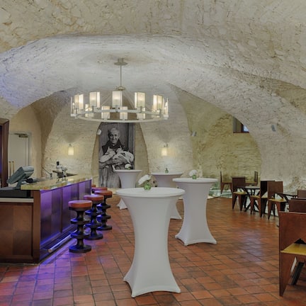 A restaurant with a rustic stone ceiling, white round tables, and a bar area with stools.