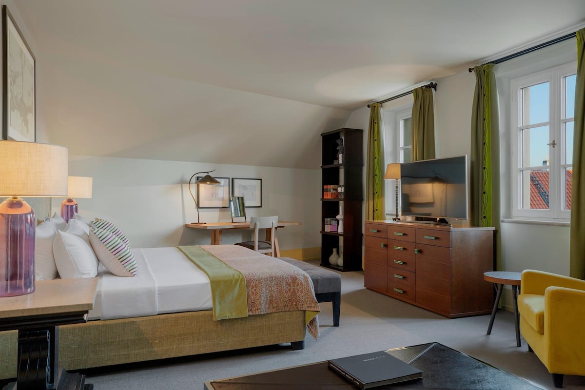 A hotel room with a bed, desk, chair, TV, wardrobe, and a small table.