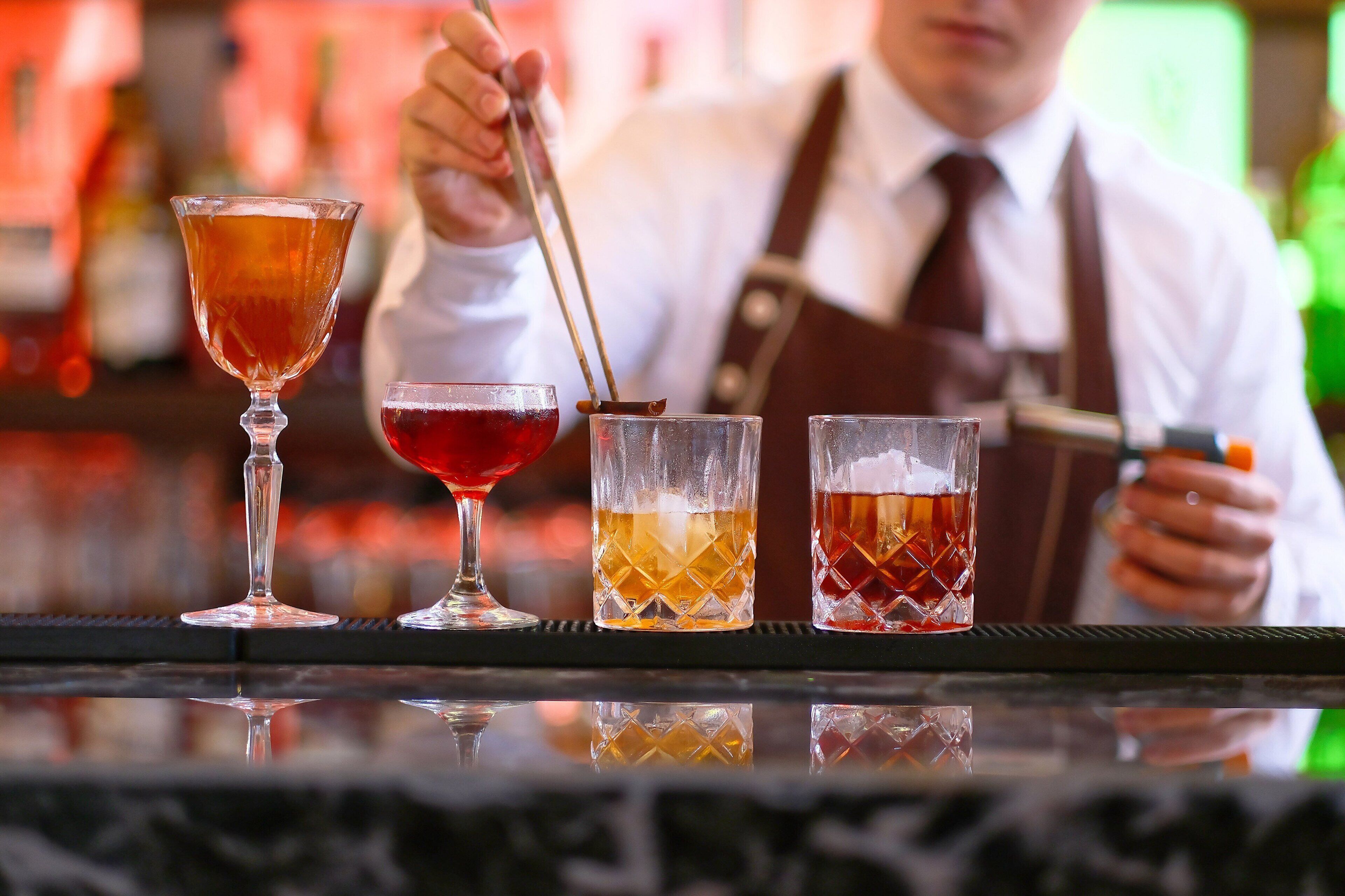 Ein Barkeeper bereitet Getränke an der Bar zu, neben ihm drei Gläser mit verschiedenen Getränken.