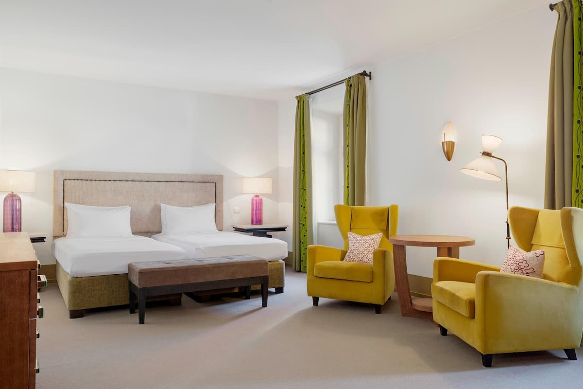 A hotel room with a bed, two chairs, a small table, and a lamp.