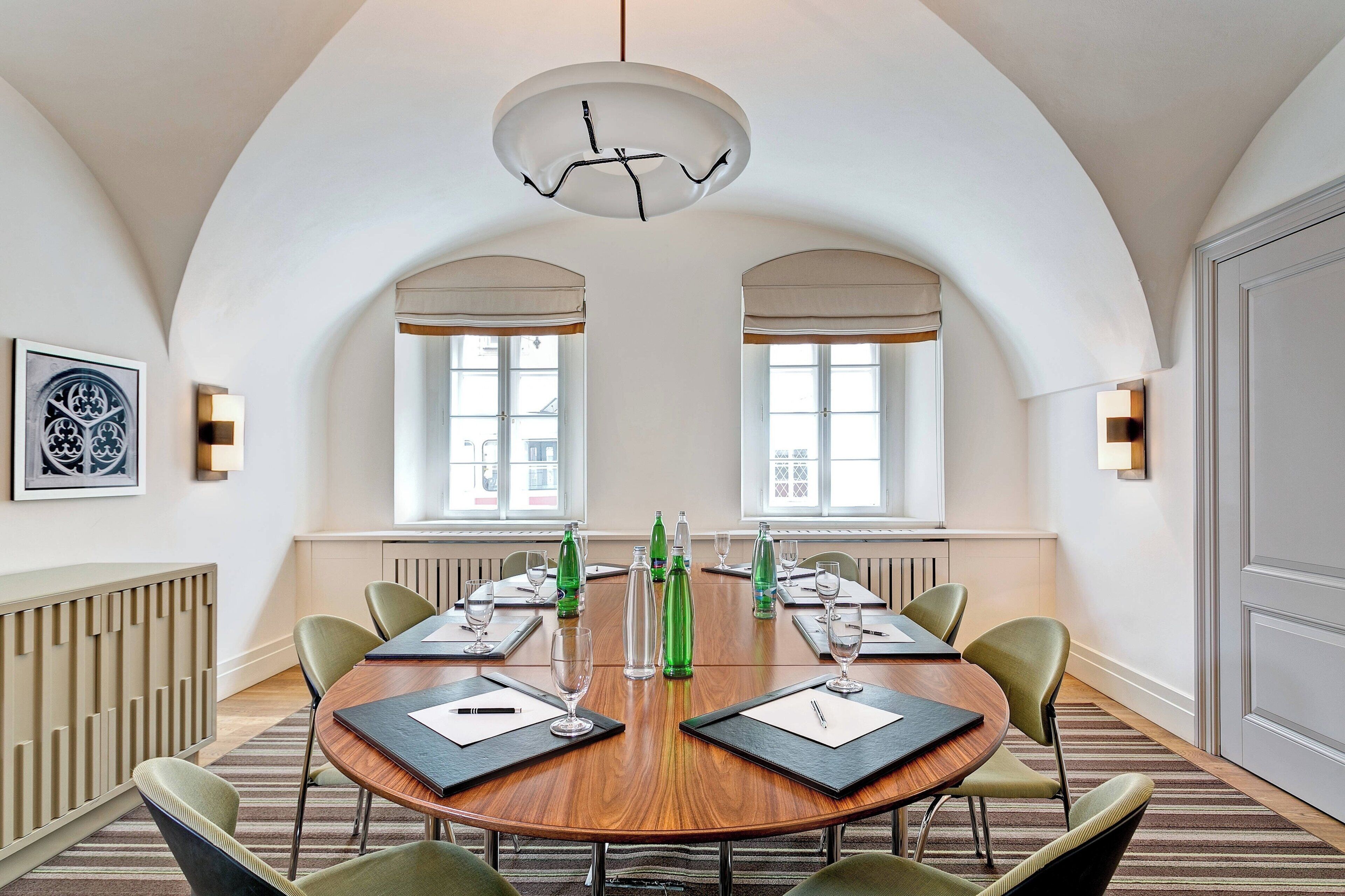 A conference room with a round wooden table, green chairs, and a modern chandelier.