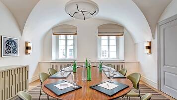 A conference room with a round wooden table, green chairs, and a modern chandelier.
