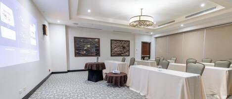 Una sala de conferencias con mesas, sillas, una pantalla de proyector y una araña.