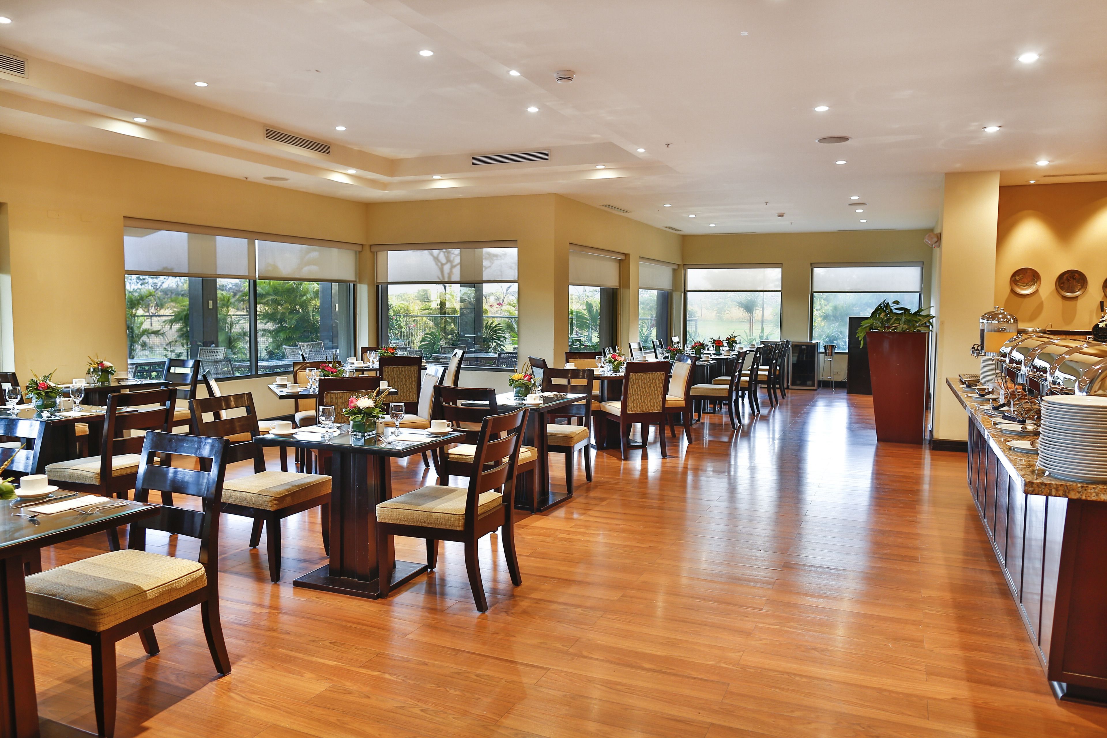 A spacious dining area with multiple tables and chairs, large windows, and a buffet counter.