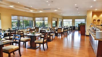 A spacious dining area with multiple tables and chairs, large windows, and a buffet counter.