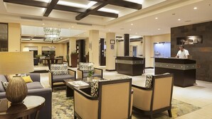 A hotel lobby with seating areas, a reception desk, and a chandelier.
