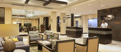 Un hall de hotel con áreas de descanso, un mostrador de recepción y un candelabro.