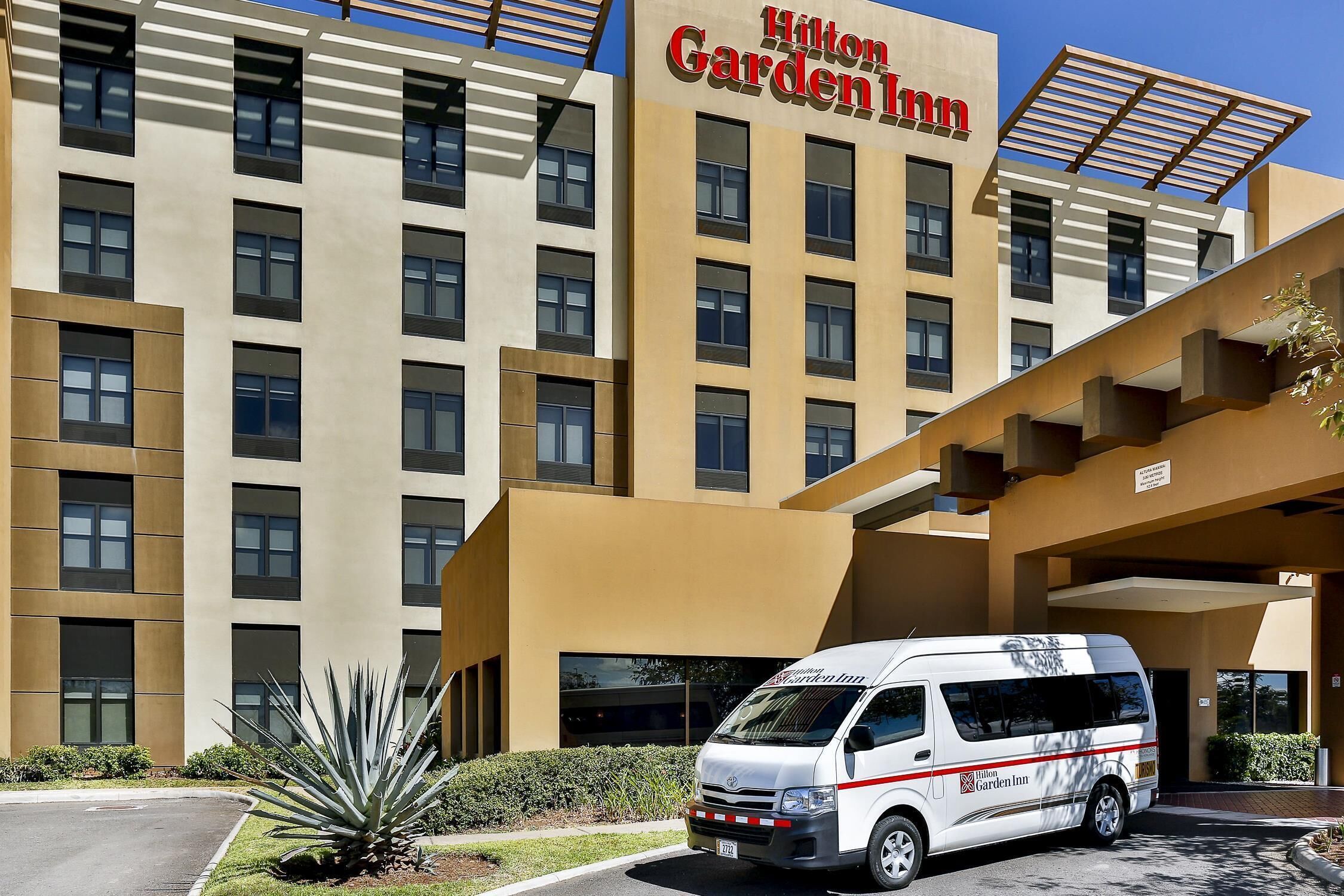 Un hotel Hilton Garden Inn con fachada moderna, una furgoneta estacionada al frente y un césped bien cuidado.