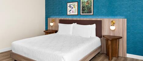 A hotel room with a large bed, wooden headboard, two wall-mounted nightstands, and two framed pictures above the bed.