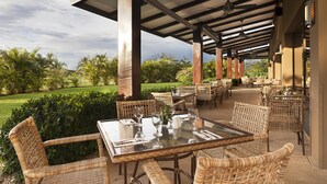 An outdoor patio area with wicker furniture, glass tables, and a view of a well-maintained garden.