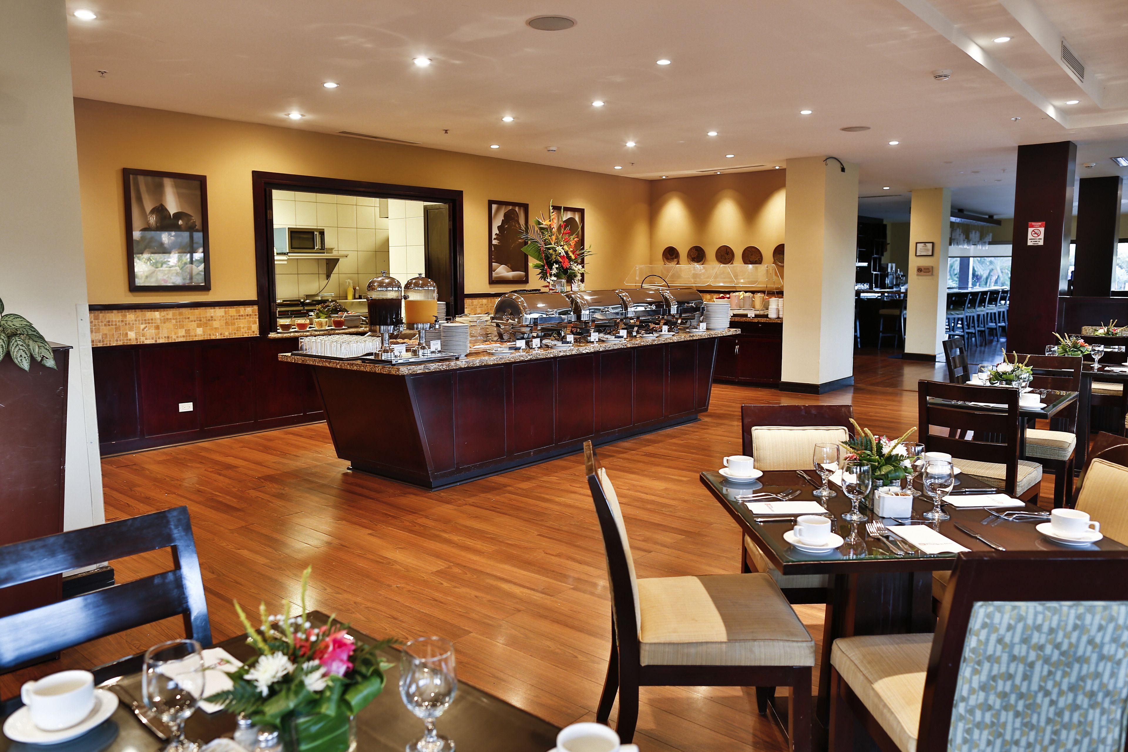 A hotel dining area with a buffet, wooden flooring, and tables set for dining.