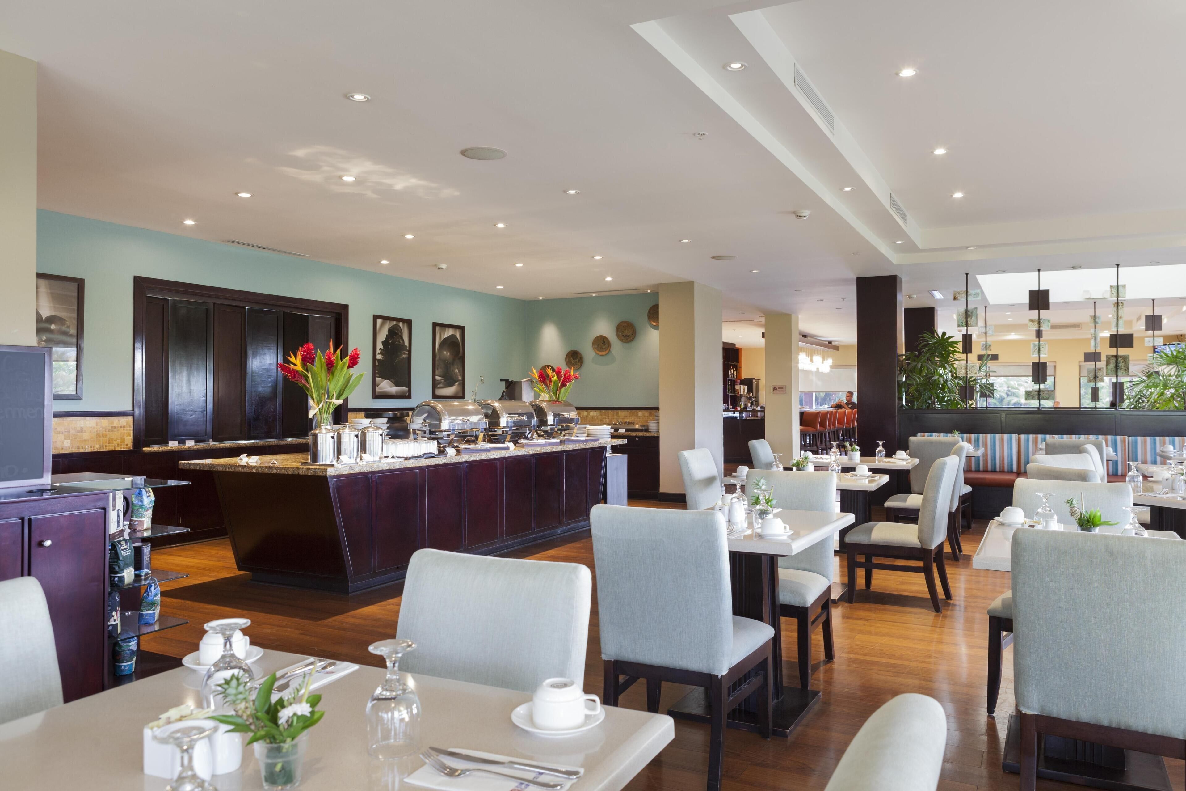 Ein modernes Restaurant mit einer zentralen Bar, Esstischen und Stühlen.