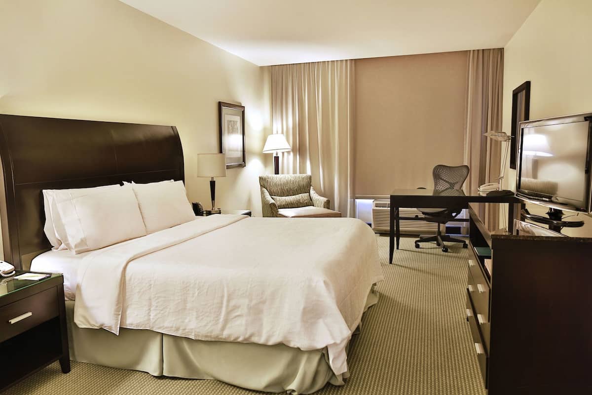 Une chambre d’hôtel avec un grand lit, un bureau avec une chaise, une télévision et une lampe.